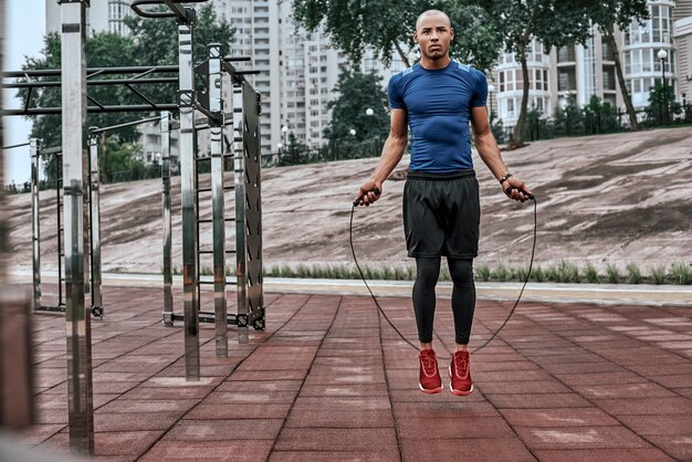 L'homme africain musclé saute le portrait de corde d'un jeune homme musclé faisant de l'exercice