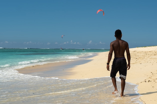 Un homme africain sur une plage tropicale se promène le long du rivage