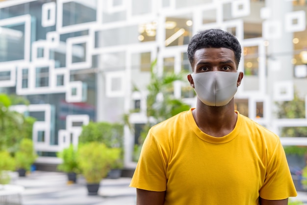 Photo homme africain portant un t-shirt jaune et un masque facial pour se protéger du coronavirus covid-19 à l'extérieur de la ville