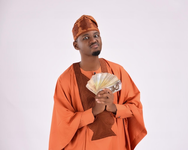 Homme africain portant une tenue traditionnelle Yoruba agbada tenant un paquet d'argent naira nigérian look avare