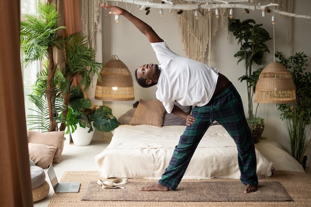 Homme africain pratiquant le yoga faisant la pose de trikonasana ou de triangle à la maison