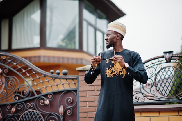 Homme Africain Riche En Vêtements Traditionnels élégants Et Chapeau Posé Fond Extérieur Son Manoir.