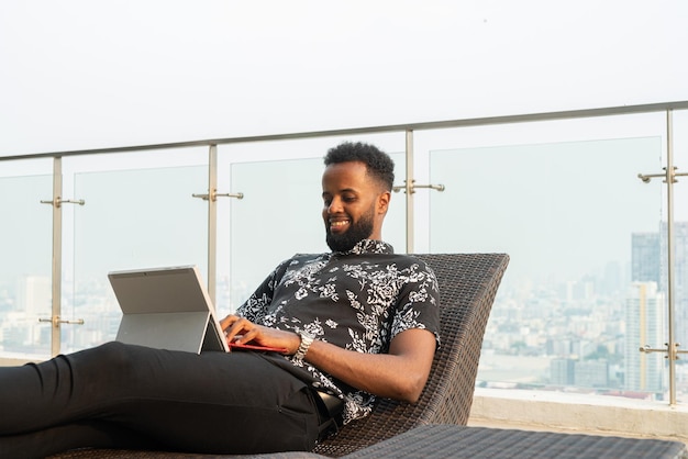 Homme africain se relaxant à l'extérieur tout en utilisant un ordinateur portable et un téléphone portable