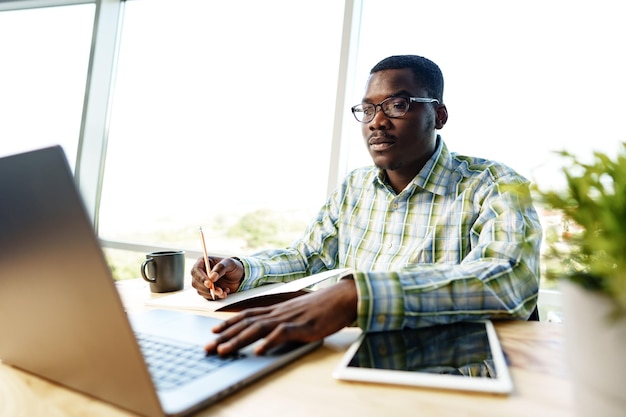 Homme africain sérieux et concentré étudiant ou travaillant avec un ordinateur portable à l'intérieur