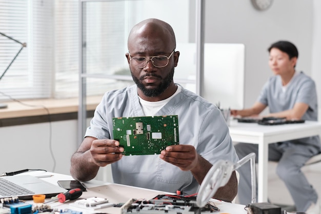 Homme africain sérieux dans les vêtements de travail regardant la carte mère dans les mains