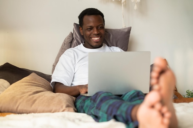 Homme africain surfant sur Internet dans son lit Travail à domicile en quarantaine Concept de distanciation sociale