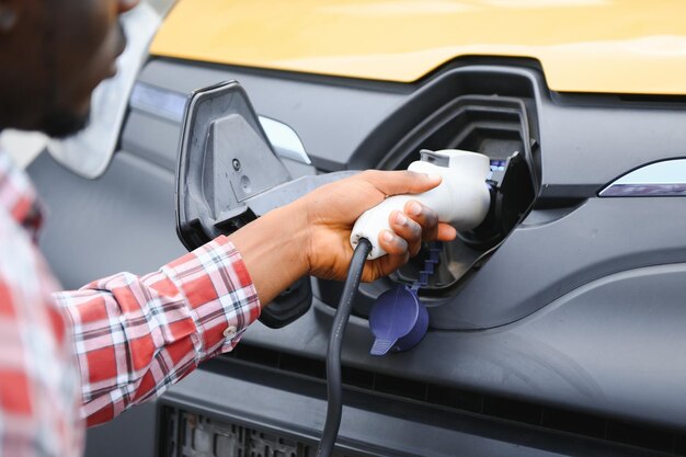 homme africain tenant un câble de charge à la main debout près d'une voiture électrique