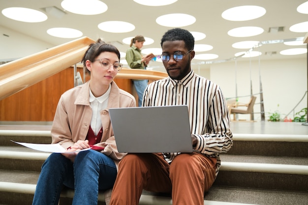 Homme africain utilisant un ordinateur portable et étudiant avec une femme alors qu'ils étaient assis dans les escaliers de la bibliothèque