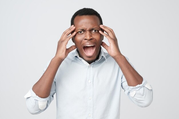 Homme afro-américain agacé en chemise bleue criant de panique choqué d'entendre de mauvaises nouvelles S