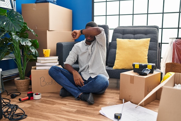 Homme afro-américain assis sur le sol dans une nouvelle maison couvrant les yeux avec le bras, l'air sérieux et triste. concept aveugle, de dissimulation et de rejet