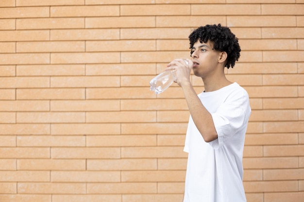 Un homme afro-américain aux cheveux bouclés qui boit de l'eau d'une bouteille en plastique transparent à la recherche de suite