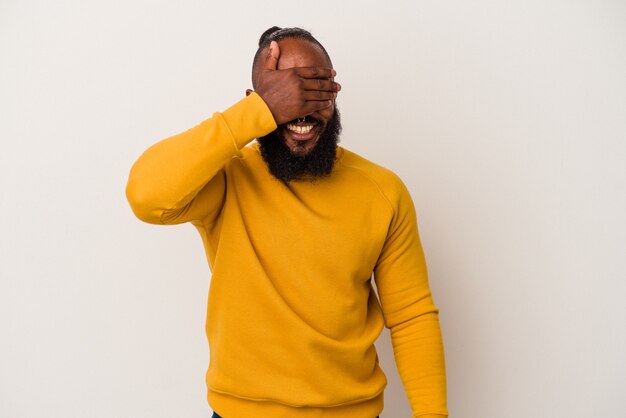 L'homme afro-américain à la barbe isolé sur fond rose couvre les yeux avec les mains, sourit largement en attendant une surprise.