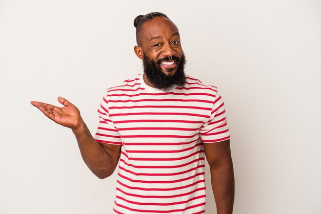 Homme afro-américain avec barbe isolé sur fond rose montrant un espace de copie sur une paume et tenant une autre main sur la taille.