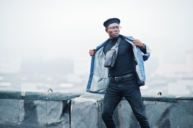 Homme afro-américain en béret veste jeans et lunettes posées sur un toit abandonné