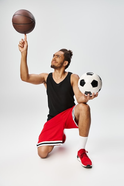 un homme afro-américain de bonne apparence posant avec du basket-ball et du football sur un fond gris