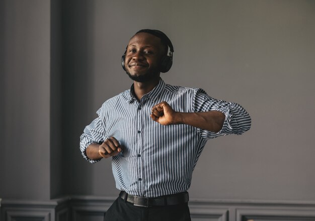 Homme afro-américain en chemise élégante dans les écouteurs, écouter de la musique et profiter de la musique, danser