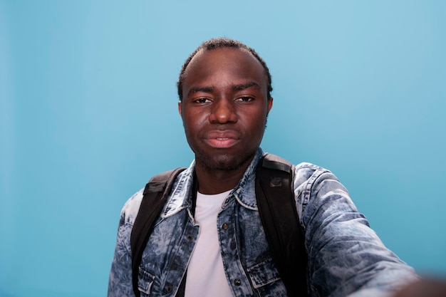 Homme Afro-américain Confiant Prenant Une Photo De Selfie Avec Un Appareil Photo Professionnel En Se Tenant Debout Sur Fond Bleu. Jeune Adulte Bel Homme Prenant Une Photo De Lui-même. Prise De Vue En Studio