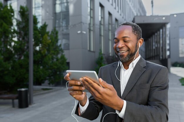 Homme afro-américain en costume d'affaires à l'extérieur d'un immeuble de bureaux regardant une vidéo en ligne avec l'application