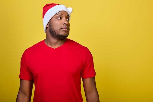 L'homme afro-américain dans un chapeau de père Noël regarde avec confiance sur le côté sur fond jaune