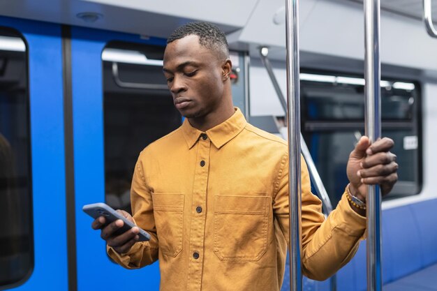 Un homme afro-américain dans une chemise élégante passe du temps au téléphone tout en conduisant dans un wagon de métro