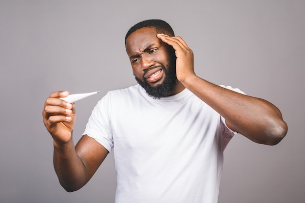 Homme afro-américain debout sur fond gris isolé, maladie et fièvre, grippe et rhume, virus malade, à l'aide d'un thermomètre.