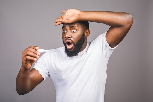 Homme afro-américain debout sur fond gris isolé Toucher le front pour la maladie et la fièvre, la grippe et le rhume, les virus malades, à l'aide d'un thermomètre.