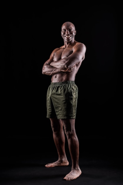 Homme afro-américain debout en short avec les bras croisés sur fond noir