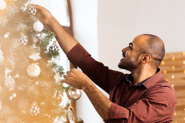 Homme afro-américain décorant le sapin de Noël à la maison