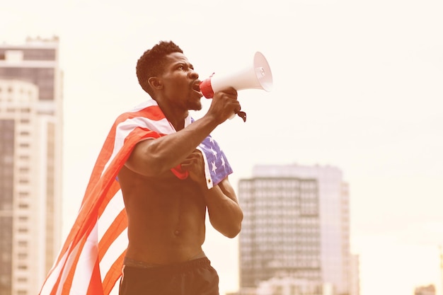 Un homme afro-américain avec le drapeau américain crie dans un mégaphone et proteste