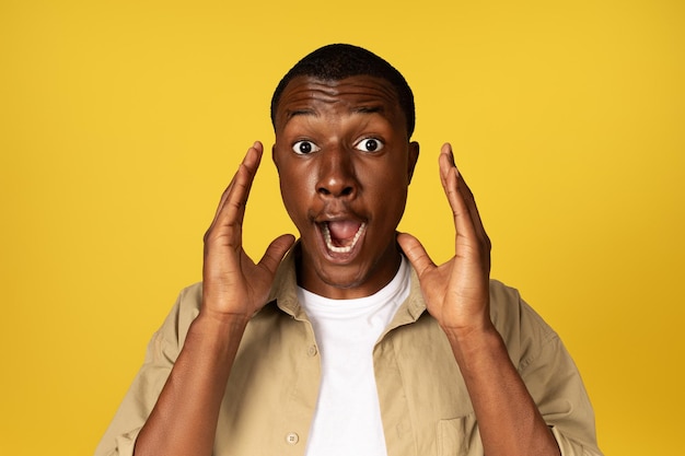 Un homme afro-américain du millénaire choqué, décontracté, avec la bouche ouverte, lève les mains en criant isolé sur