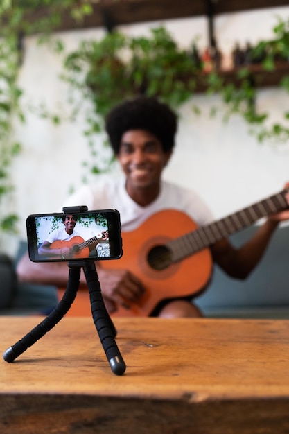 Homme afro-américain enregistrant une leçon de guitare en ligne avec un téléphone portable Mise au point sélective sur le téléphone