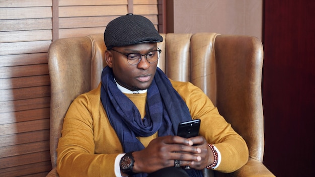 Homme afro-américain est assis sur une chaise dans un café avec des smartphones dans ses mains