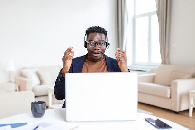 Homme afro-américain excité portant des écouteurs lisant de bonnes nouvelles dans un e-mail obtenant une nouvelle promotion d'emploi à l'aide d'un ordinateur portable regardant l'écran et criant de joie montrant oui geste célébrant