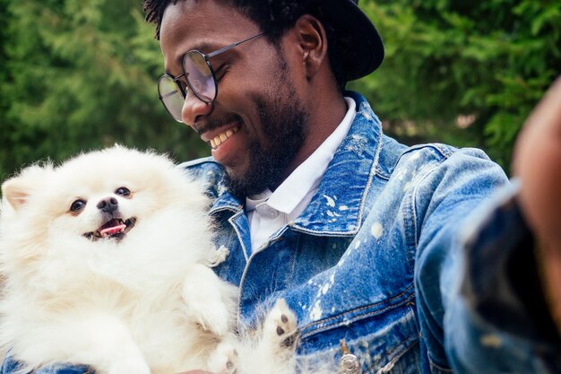 Homme afro-américain faisant un autoportrait avec un spitz moelleux dans le parc du printemps de l'été.