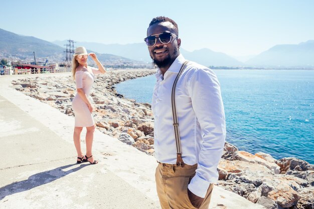 Un homme afro-américain et une femme se regardent avec amour dans un café tropical d'été et boivent un cocktail de fruits frais à l'orange.