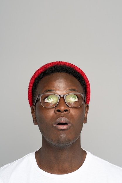 Homme afro-américain hipster porter un chapeau rouge à lunettes porter la pensée, lève les yeux dans la surprise isolée