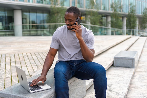 Photo un homme afro-américain indépendant utilisant un ordinateur portable parlant au téléphone dans une rue urbaine en ville un homme d'affaires