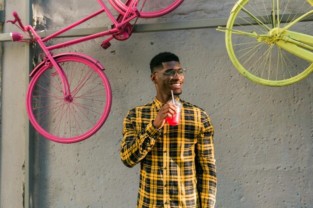 Homme afro-américain insouciant en tenue décontractée tenant un cocktail tropical fond d'été urbain cool