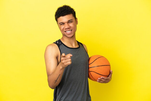 Homme afro-américain isolé sur fond jaune jouant au basket-ball et pointant vers l'avant