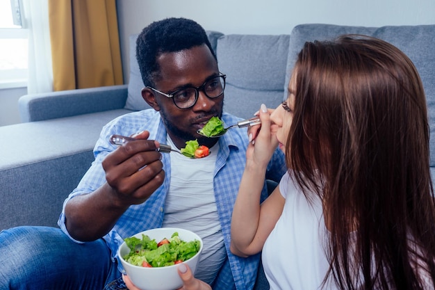 Homme afro-américain mangeant de la salade avec une femme dans le salon