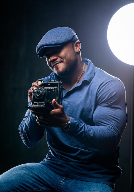 Un homme afro-américain mignon et beau photographie quelqu'un avec un appareil photo rétro Lampe lumineuse derrière le mâle Vêtements décontractés sur un homme