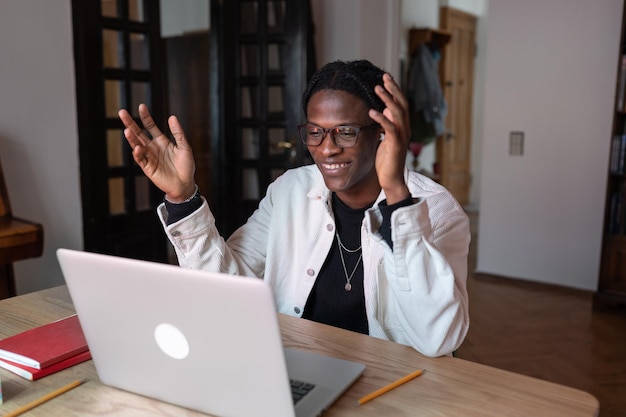 Un homme afro-américain optimiste souriant agite la main en faisant un appel vidéo sur un ordinateur portable avec des amis