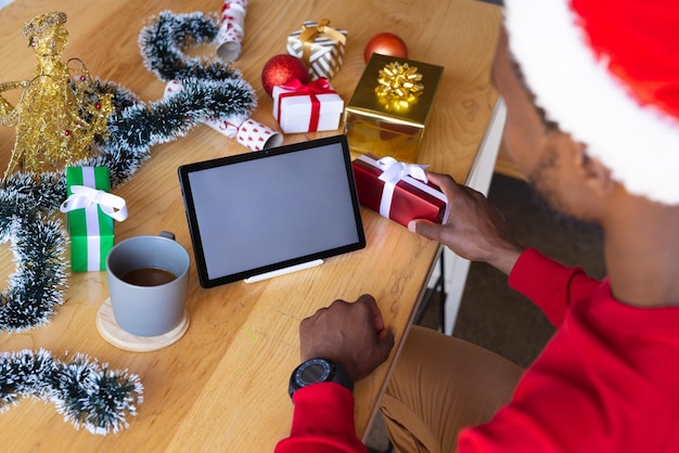 Homme afro-américain portant un chapeau de Père Noël, utilisant une tablette avec fond