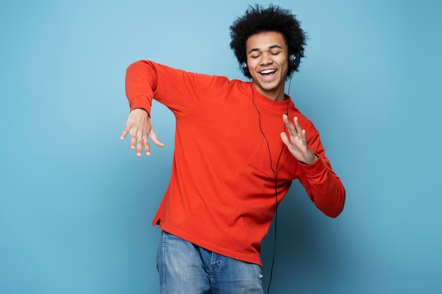 Homme afro-américain portant des écouteurs écoutant de la musique, dansant, s'amusant isolé sur fond