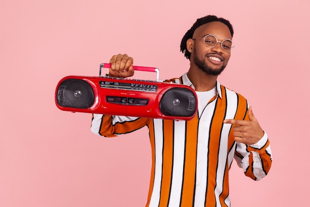 Homme afro-américain positif pointant le doigt sur un tourne-disque audio rouge vintage, profitant de la musique