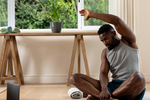 Photo un homme afro-américain pratiquant le yoga en utilisant un ordinateur portable à la maison