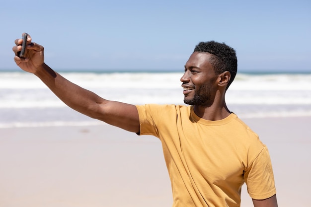 Homme afro-américain prenant un selfie avec un smartphone sur une plage au bord de la mer. mode de vie sain, loisirs dans la nature.