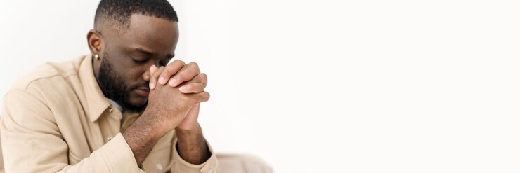 Homme afro-américain priant pour la paix assis sur le canapé à la maison Bannière Web