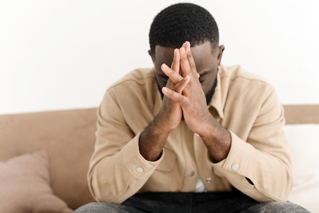 Homme afro-américain priant pour la paix assis sur le canapé à la maison