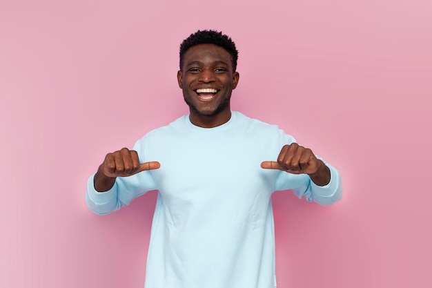 homme afro-américain en pull bleu pointe avec ses mains sur lui-même sur fond rose isolé